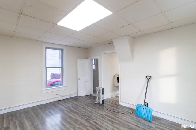 interior space featuring a drop ceiling, wood finished floors, baseboards, heating unit, and radiator heating unit