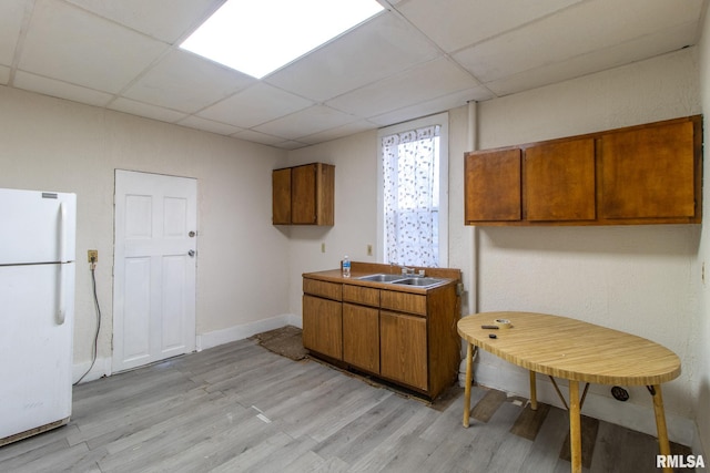 kitchen featuring a paneled ceiling, brown cabinetry, a sink, and freestanding refrigerator