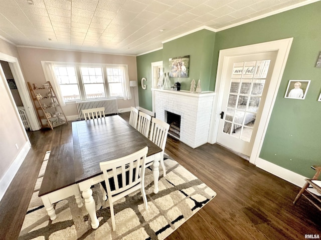 dining space with dark hardwood / wood-style floors, ornamental molding, and a brick fireplace