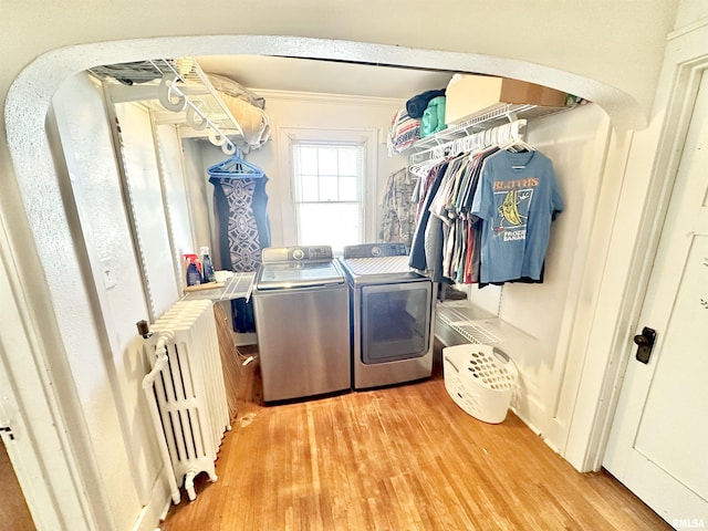 laundry room featuring radiator, washer and clothes dryer, ornamental molding, and light hardwood / wood-style flooring