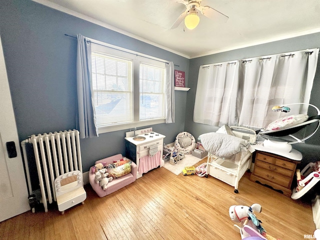 interior space featuring radiator, ceiling fan, crown molding, and wood-type flooring