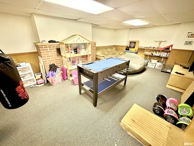 rec room with carpet flooring, a paneled ceiling, and wood walls