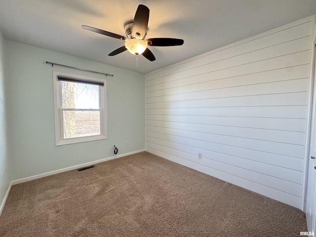 unfurnished room featuring carpet floors, ceiling fan, and wood walls