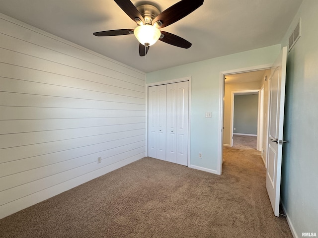 unfurnished bedroom featuring ceiling fan, a closet, wood walls, and carpet flooring