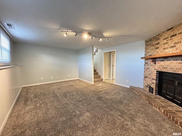 unfurnished living room with carpet floors, a brick fireplace, and track lighting