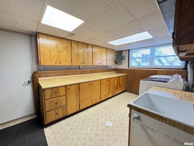 kitchen featuring wood walls, washing machine and clothes dryer, electric panel, a drop ceiling, and sink