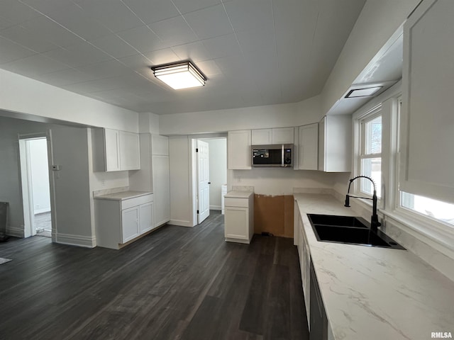 kitchen featuring dark wood-style floors, stainless steel microwave, white cabinets, a sink, and light stone countertops