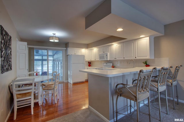 kitchen featuring a kitchen breakfast bar, kitchen peninsula, light hardwood / wood-style floors, white appliances, and white cabinets