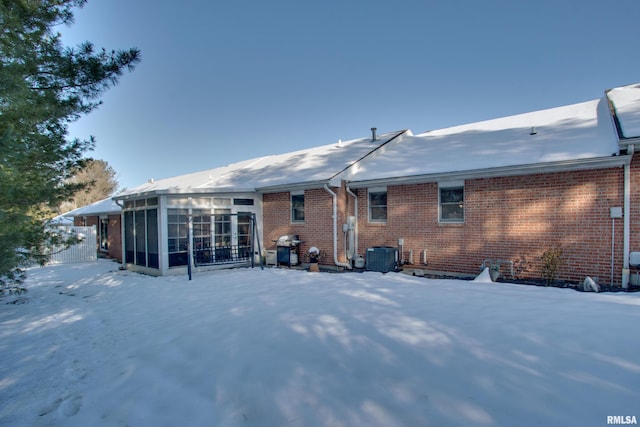 snow covered rear of property featuring a sunroom and cooling unit