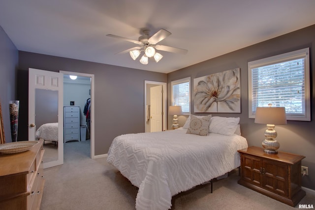 bedroom with light carpet, a walk in closet, ceiling fan, multiple windows, and a closet