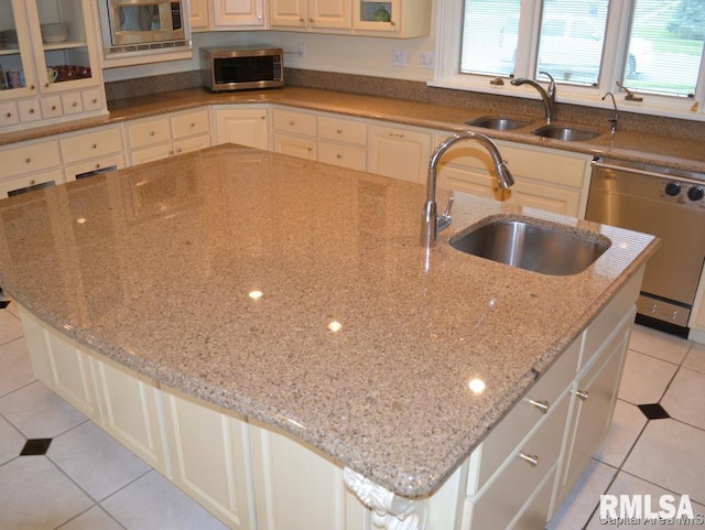 kitchen featuring light tile patterned floors, stainless steel appliances, a sink, and a kitchen island with sink