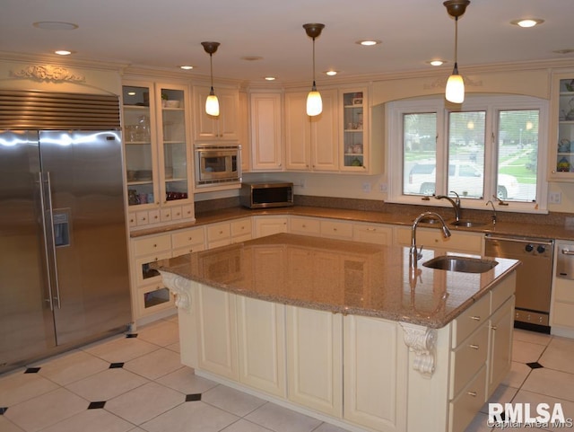 kitchen featuring stone countertops, hanging light fixtures, a kitchen island with sink, stainless steel appliances, and a sink