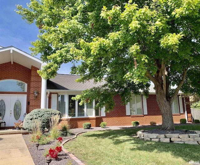 view of front of house with roof with shingles, a front yard, and brick siding