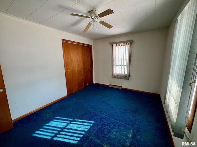 unfurnished bedroom with baseboard heating, ceiling fan, a closet, and dark carpet