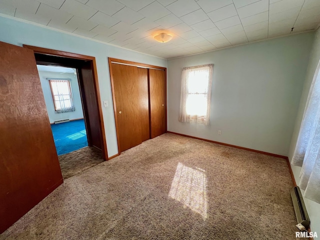 unfurnished bedroom with a closet, carpet floors, and a baseboard heating unit