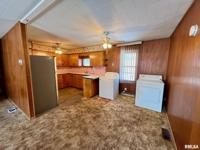 kitchen with stainless steel refrigerator, sink, wooden walls, light carpet, and washer and dryer