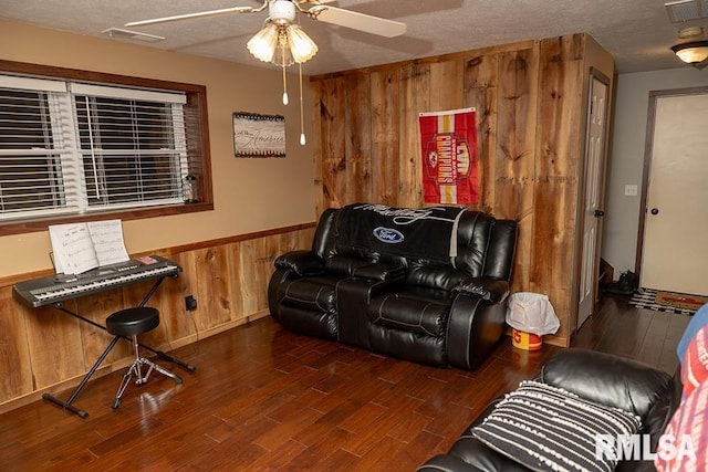 living room with a textured ceiling, wood walls, ceiling fan, and dark hardwood / wood-style floors