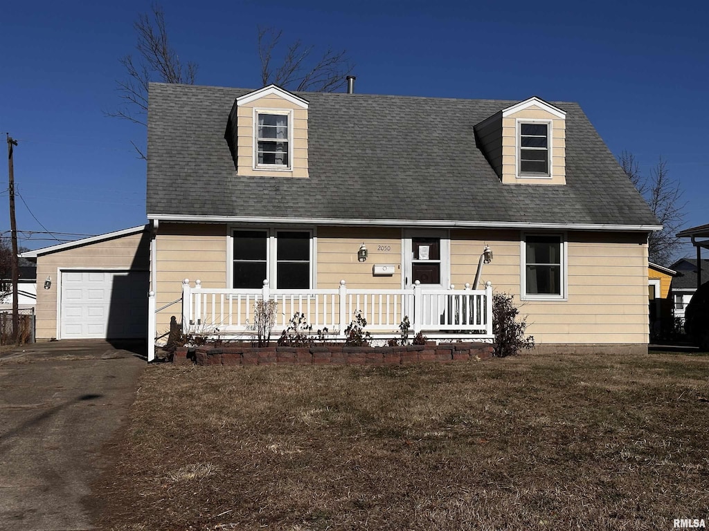 new england style home with an attached garage, covered porch, a shingled roof, driveway, and a front lawn