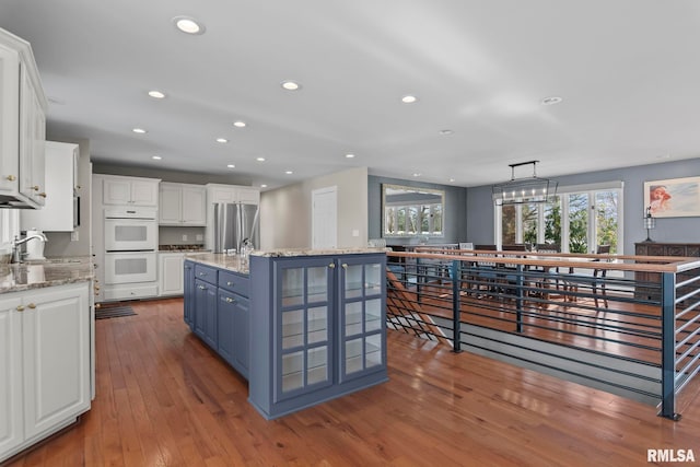 kitchen featuring blue cabinets, decorative light fixtures, stainless steel fridge, a kitchen island with sink, and white cabinets