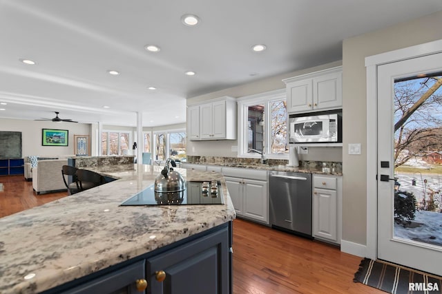 kitchen with sink, appliances with stainless steel finishes, light stone counters, wood-type flooring, and white cabinets