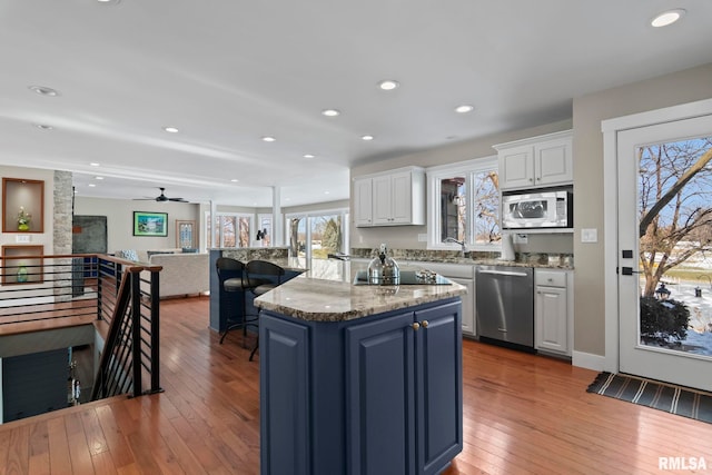 kitchen with blue cabinetry, white cabinetry, appliances with stainless steel finishes, a kitchen island, and hardwood / wood-style flooring