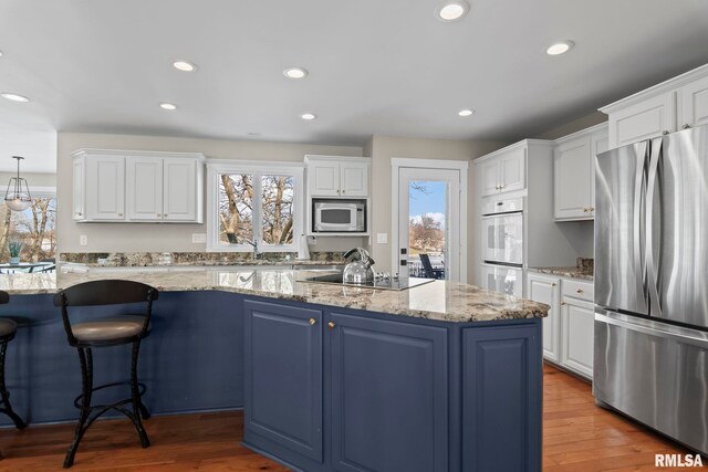 kitchen featuring white cabinetry, stainless steel appliances, a center island with sink, and plenty of natural light