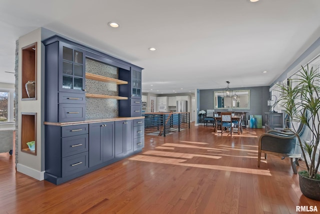 interior space featuring blue cabinets, an inviting chandelier, wood-type flooring, hanging light fixtures, and stainless steel fridge