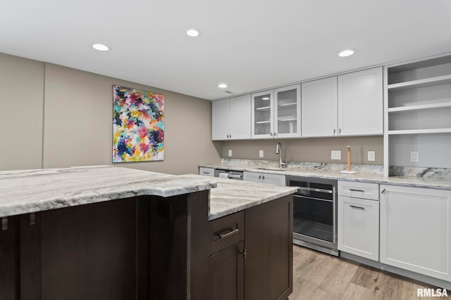 kitchen featuring sink, white cabinets, beverage cooler, light stone counters, and light hardwood / wood-style flooring