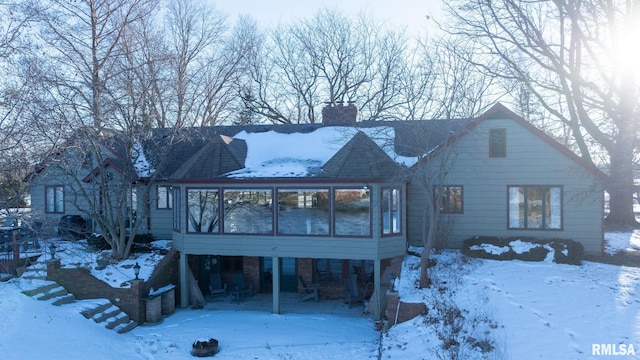 snow covered rear of property with a sunroom