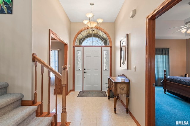 foyer entrance featuring light tile patterned floors, baseboards, stairway, and ceiling fan with notable chandelier