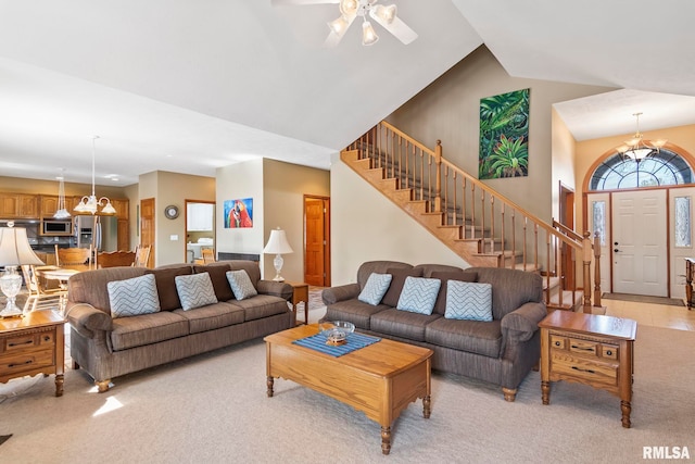 living area featuring light carpet, a high ceiling, stairway, and ceiling fan with notable chandelier