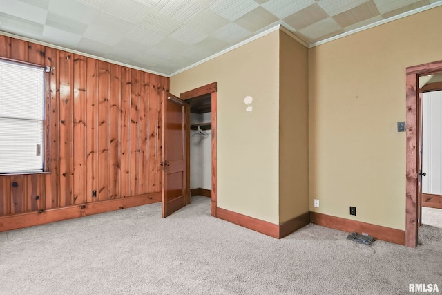 unfurnished bedroom featuring wooden walls, a closet, crown molding, and light colored carpet