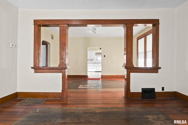 spare room featuring decorative columns and dark hardwood / wood-style floors