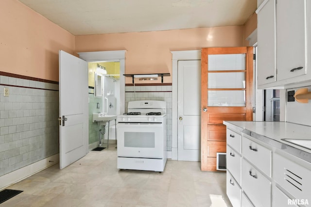 kitchen featuring tile walls, white cabinets, and white range with gas cooktop