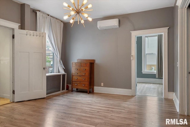 unfurnished bedroom featuring a wall unit AC, a chandelier, and light hardwood / wood-style flooring