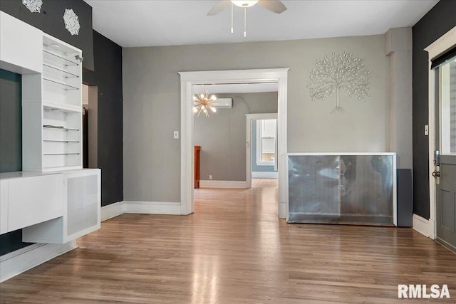 unfurnished living room featuring a wall mounted air conditioner, ceiling fan with notable chandelier, hardwood / wood-style floors, and built in features