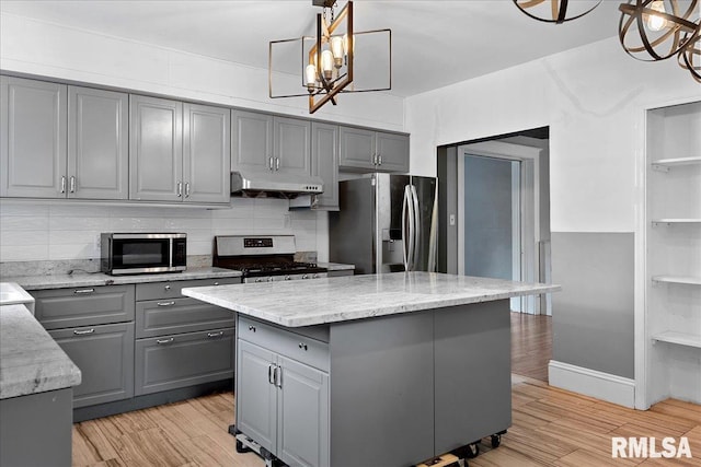 kitchen featuring light stone counters, a center island, decorative light fixtures, stainless steel appliances, and gray cabinets