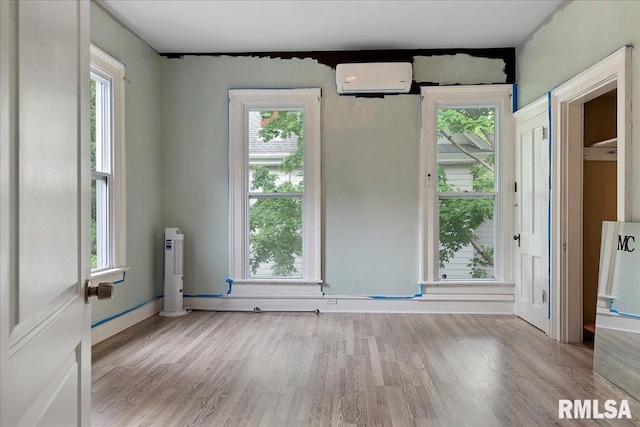 spare room featuring light hardwood / wood-style floors, a healthy amount of sunlight, and a wall mounted AC