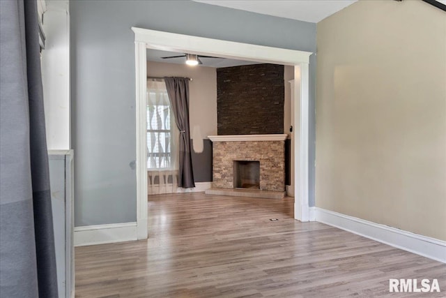 unfurnished living room with light hardwood / wood-style floors, ceiling fan, and a stone fireplace