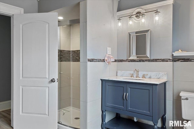 bathroom featuring toilet, hardwood / wood-style flooring, walk in shower, tile walls, and vanity