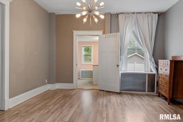 unfurnished bedroom with an inviting chandelier, multiple windows, and light wood-type flooring