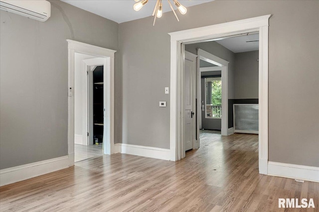 unfurnished room featuring an AC wall unit, light hardwood / wood-style floors, and a notable chandelier