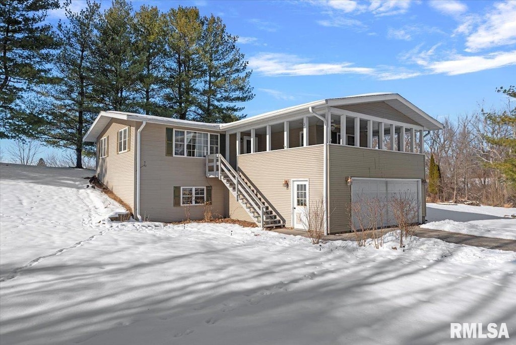 snow covered rear of property featuring a sunroom and a garage