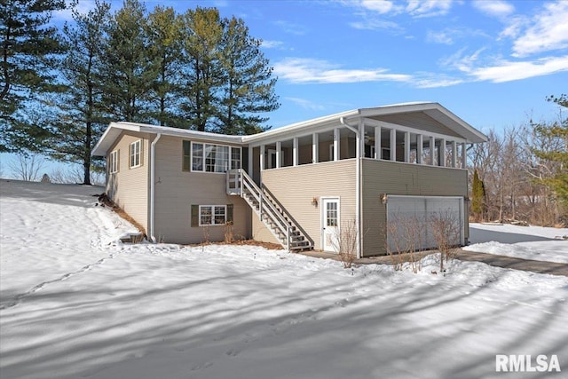 snow covered rear of property featuring a sunroom and a garage