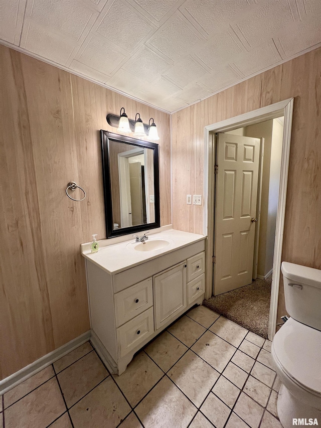 bathroom featuring toilet, vanity, wood walls, and tile patterned flooring