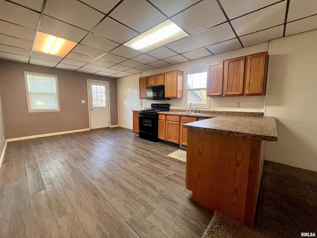 kitchen featuring plenty of natural light, a drop ceiling, wood-type flooring, and black appliances