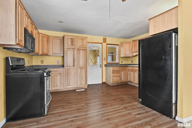 kitchen featuring light brown cabinets, wood finished floors, baseboards, black appliances, and dark countertops