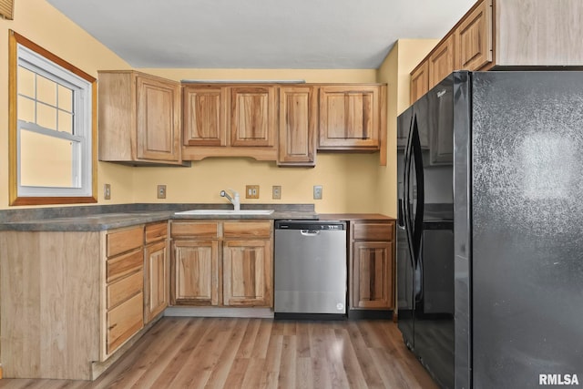 kitchen with dishwasher, dark countertops, light wood-style flooring, black fridge, and a sink