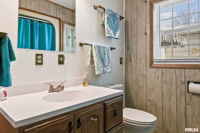 bathroom featuring toilet, wooden walls, and vanity