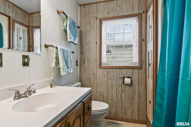 full bathroom featuring toilet, vanity, visible vents, and wooden walls